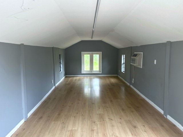 additional living space featuring lofted ceiling, light wood-type flooring, and a wall unit AC