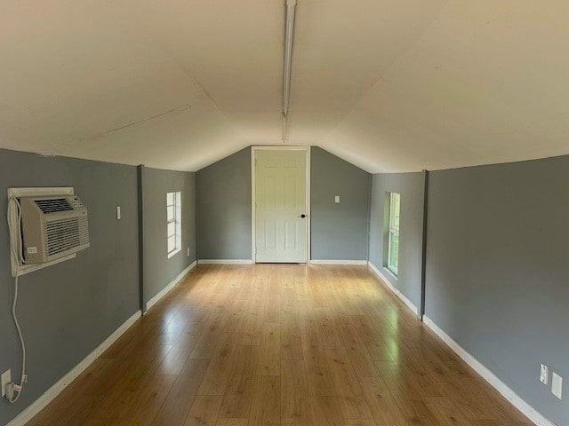 additional living space featuring light hardwood / wood-style floors, an AC wall unit, and lofted ceiling