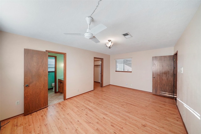 unfurnished bedroom featuring connected bathroom, a spacious closet, light wood-type flooring, a closet, and ceiling fan