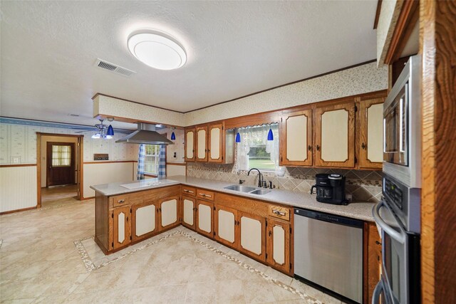 kitchen featuring sink, wall chimney range hood, appliances with stainless steel finishes, plenty of natural light, and kitchen peninsula