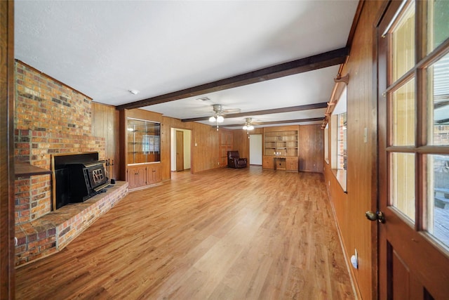 unfurnished living room with beam ceiling, light hardwood / wood-style flooring, wood walls, and a wood stove