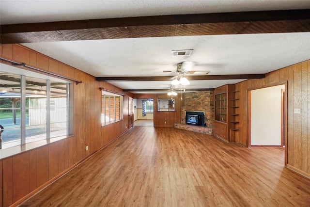 unfurnished living room featuring built in features, wood walls, beamed ceiling, wood-type flooring, and ceiling fan