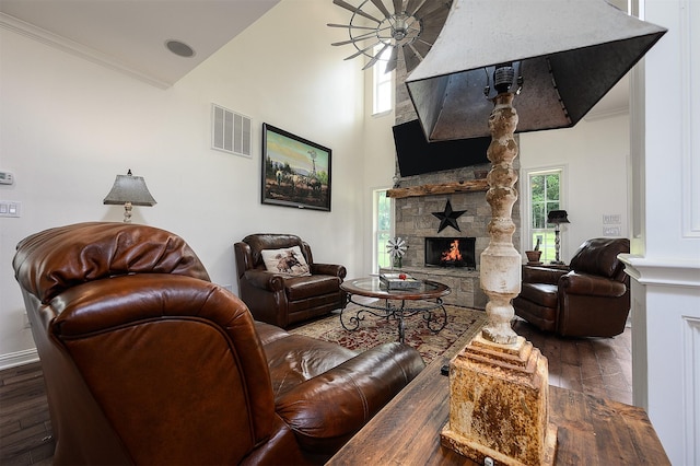 living room featuring ceiling fan, a stone fireplace, dark wood-type flooring, and crown molding