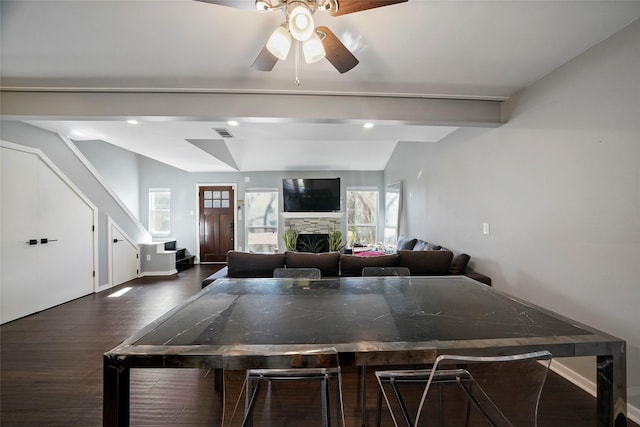 kitchen with ceiling fan, a stone fireplace, vaulted ceiling with beams, and dark hardwood / wood-style flooring