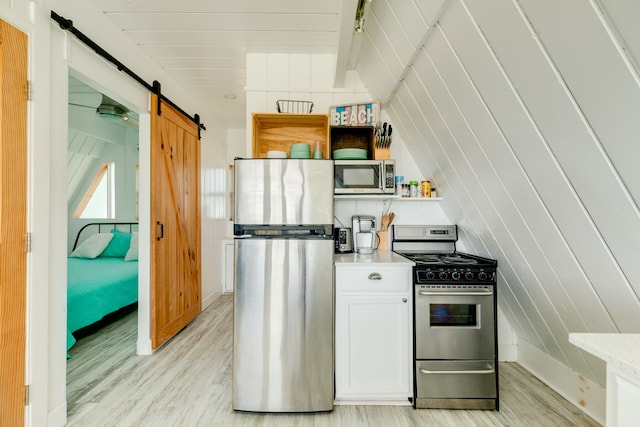 kitchen featuring a barn door, white cabinetry, light wood-type flooring, and stainless steel appliances