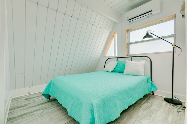 bedroom with lofted ceiling with beams, light hardwood / wood-style floors, and a wall mounted air conditioner