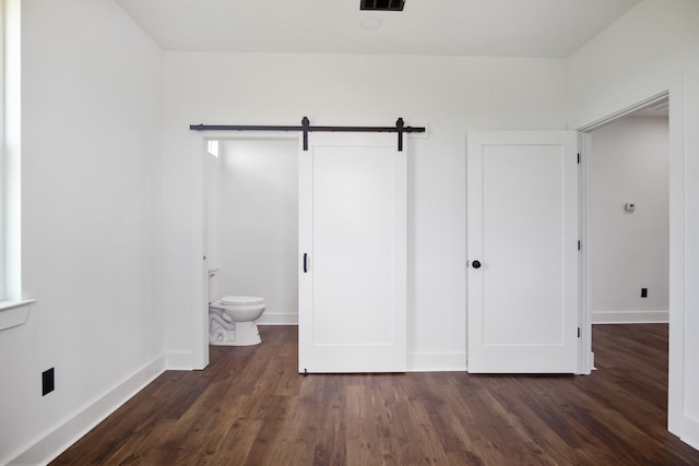 unfurnished bedroom featuring dark wood-type flooring, connected bathroom, a barn door, and a closet