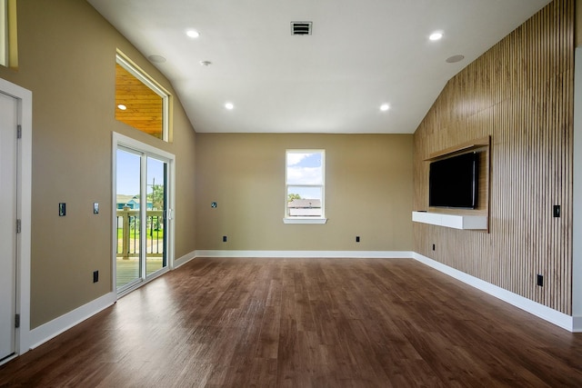 unfurnished living room featuring lofted ceiling, hardwood / wood-style floors, wooden walls, and a healthy amount of sunlight