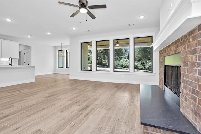 unfurnished living room featuring a brick fireplace, ceiling fan with notable chandelier, and light hardwood / wood-style flooring