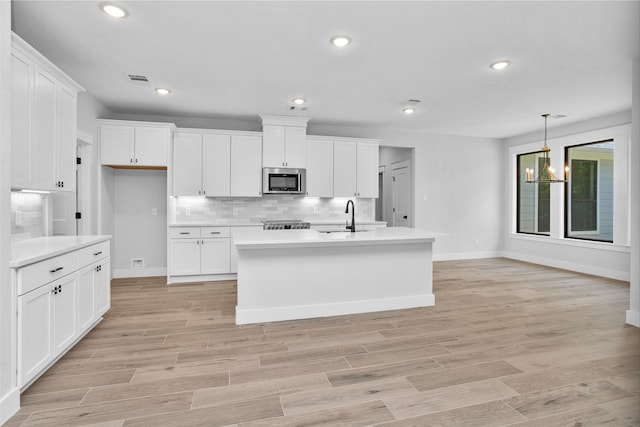 kitchen featuring white cabinetry, an island with sink, sink, and tasteful backsplash