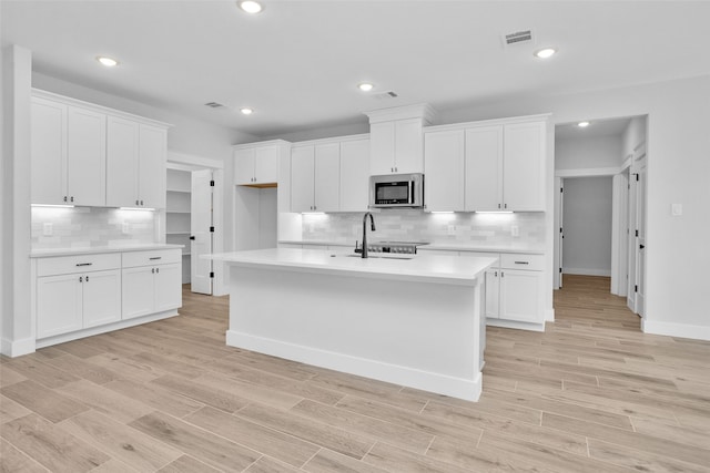 kitchen with white cabinetry, a kitchen island with sink, sink, and light wood-type flooring