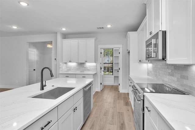 kitchen with white cabinetry, sink, light stone counters, stainless steel appliances, and light wood-type flooring