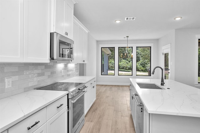 kitchen featuring white cabinetry, sink, decorative light fixtures, and appliances with stainless steel finishes