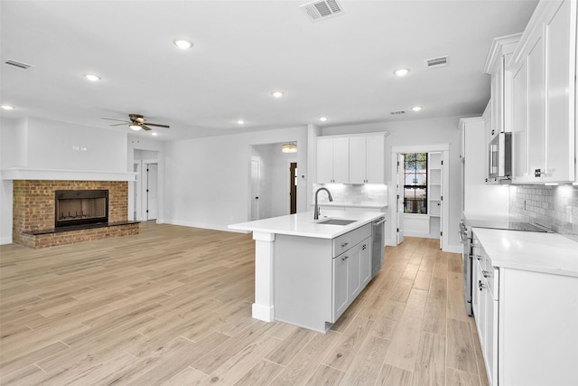 kitchen with appliances with stainless steel finishes, white cabinetry, an island with sink, sink, and light hardwood / wood-style flooring