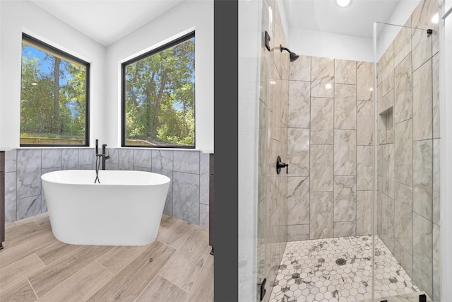 651 Paradise Dr, Coldspring, TX 77331 - bathroom with a stall shower, tile walls, a soaking tub, wood finished floors, and a wainscoted wall