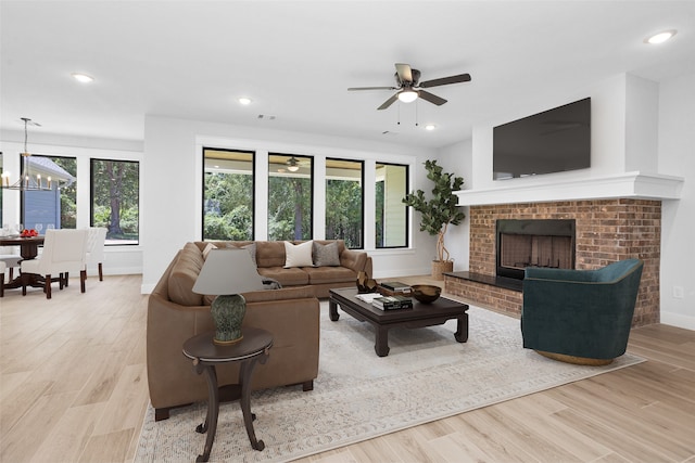 living room with a brick fireplace, ceiling fan with notable chandelier, and light hardwood / wood-style floors