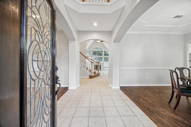 foyer featuring light tile patterned floors, visible vents, baseboards, arched walkways, and stairs