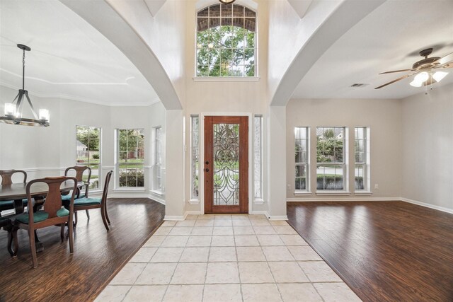 foyer entrance with a towering ceiling, crown molding, light wood-type flooring, and ceiling fan with notable chandelier