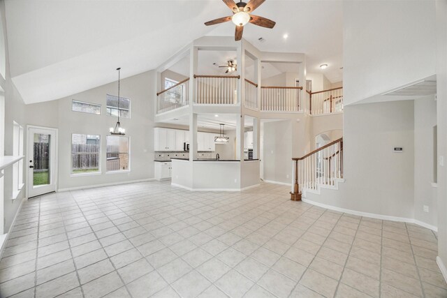 unfurnished living room with high vaulted ceiling, ceiling fan with notable chandelier, and light tile floors