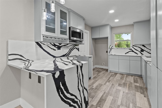 kitchen with gray cabinetry, pendant lighting, kitchen peninsula, decorative backsplash, and light wood-type flooring