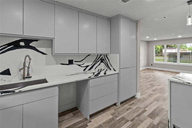 kitchen featuring tasteful backsplash, decorative light fixtures, sink, and light wood-type flooring