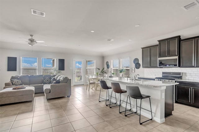 kitchen featuring a breakfast bar, a center island with sink, ceiling fan, light tile patterned floors, and appliances with stainless steel finishes