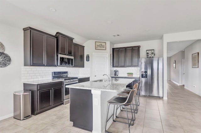 kitchen featuring backsplash, sink, light tile patterned floors, an island with sink, and appliances with stainless steel finishes