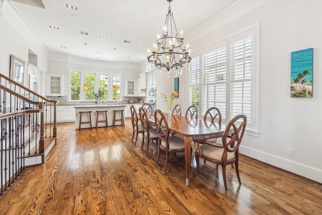 dining space with hardwood / wood-style floors, ornamental molding, and an inviting chandelier