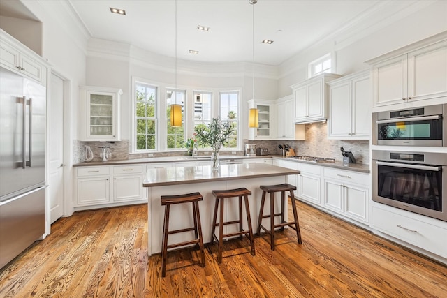 kitchen with decorative light fixtures, a breakfast bar, white cabinetry, a kitchen island with sink, and appliances with stainless steel finishes