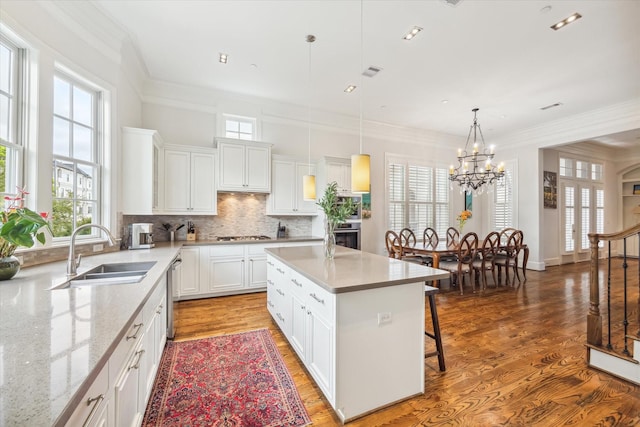 kitchen with decorative light fixtures, a kitchen island, sink, white cabinets, and a chandelier