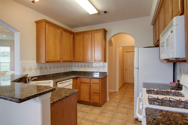 kitchen with white appliances, dark stone countertops, kitchen peninsula, and backsplash