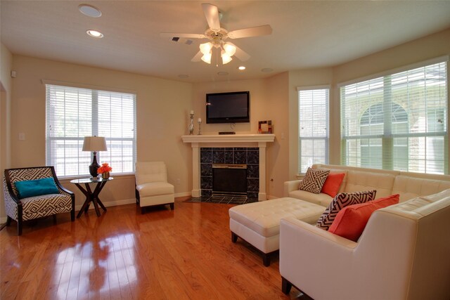 living room featuring ceiling fan, a tiled fireplace, a healthy amount of sunlight, and hardwood / wood-style floors