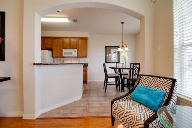 kitchen featuring dark stone counters, white appliances, light tile flooring, pendant lighting, and a notable chandelier