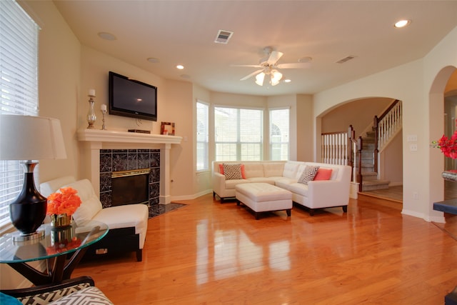 living room with ceiling fan, a tiled fireplace, and light hardwood / wood-style flooring