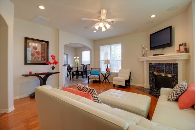 living room featuring ceiling fan, a tiled fireplace, and wood-type flooring