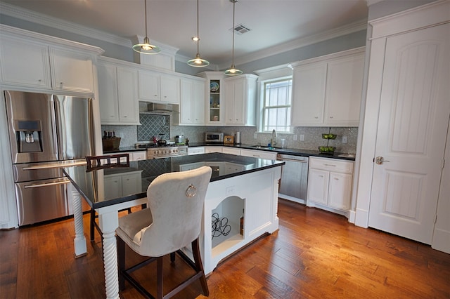 kitchen with appliances with stainless steel finishes, hanging light fixtures, wood-type flooring, and wall chimney exhaust hood