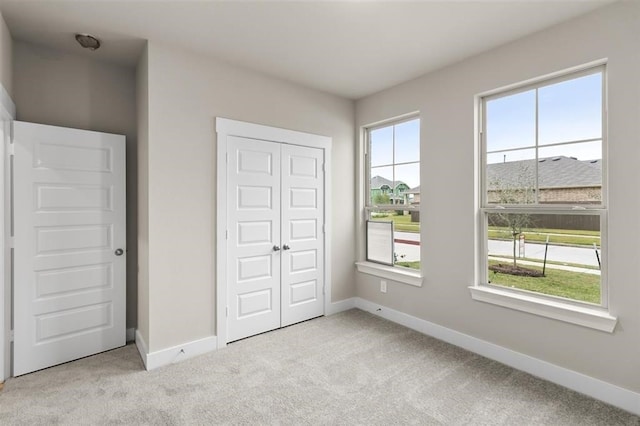 unfurnished bedroom featuring multiple windows, light carpet, and a closet