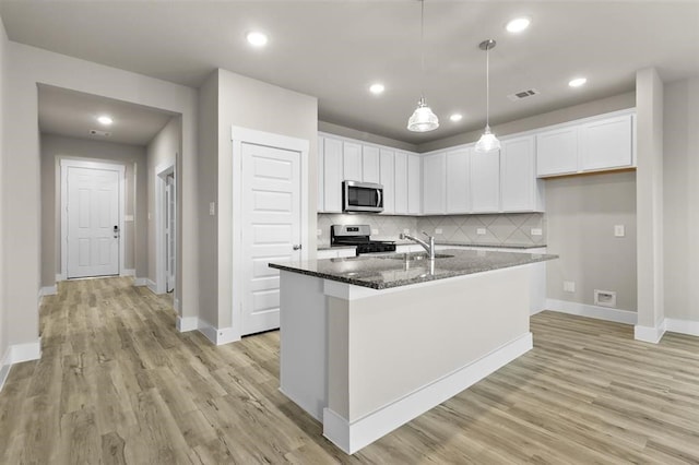 kitchen with decorative backsplash, appliances with stainless steel finishes, a center island with sink, and white cabinetry