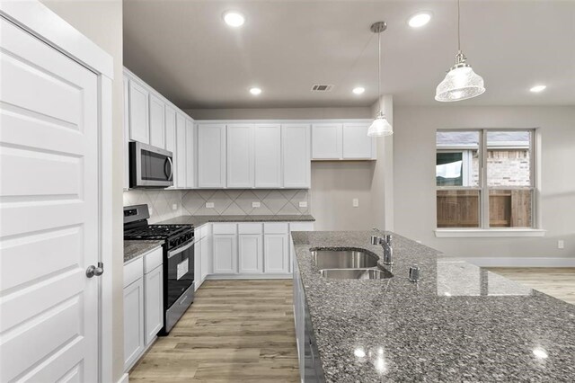 kitchen with white cabinetry, sink, hanging light fixtures, stainless steel appliances, and backsplash