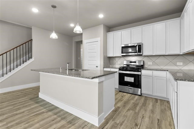 kitchen with white cabinetry, sink, stainless steel appliances, and a center island with sink