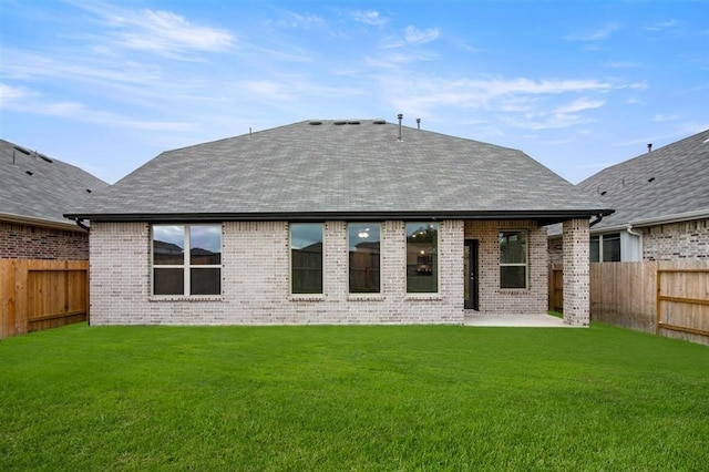 back of property with a shingled roof, a patio area, a fenced backyard, and a yard