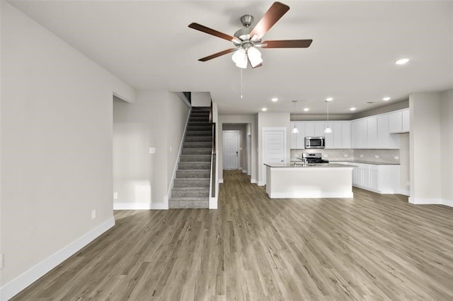 unfurnished living room featuring stairway, baseboards, a ceiling fan, and light wood finished floors