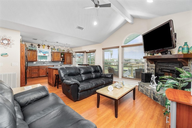 living room featuring a fireplace, lofted ceiling with beams, sink, ceiling fan, and light hardwood / wood-style flooring