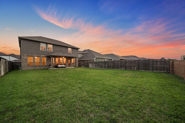 back house at dusk featuring a yard and a patio area