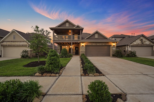 view of front of property featuring an attached garage, a balcony, driveway, stone siding, and a front lawn