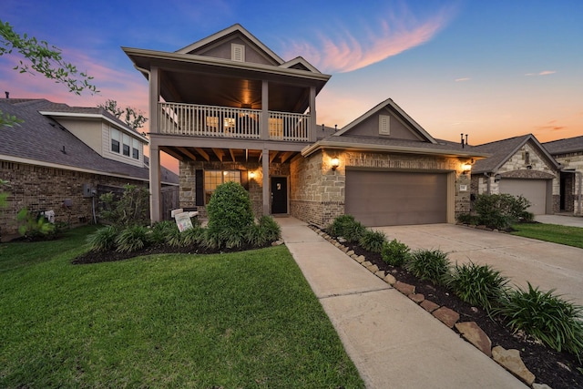 view of front of home featuring an attached garage, a balcony, concrete driveway, stone siding, and a front yard