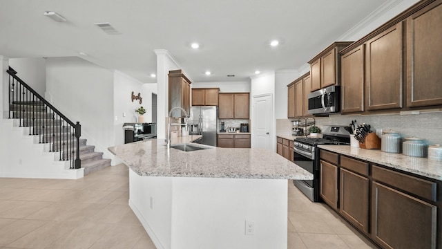 kitchen with a kitchen island with sink, light stone countertops, light tile patterned floors, tasteful backsplash, and stainless steel appliances