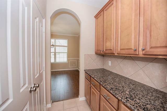 kitchen with decorative backsplash, light tile patterned flooring, dark stone countertops, and ornamental molding