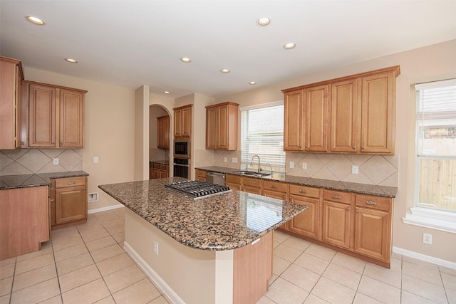 kitchen with a center island, sink, tasteful backsplash, dark stone countertops, and appliances with stainless steel finishes