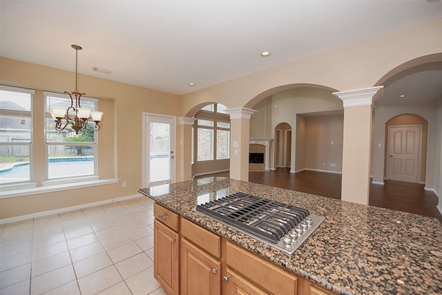 kitchen featuring light tile patterned flooring, an inviting chandelier, dark stone counters, and stainless steel gas cooktop